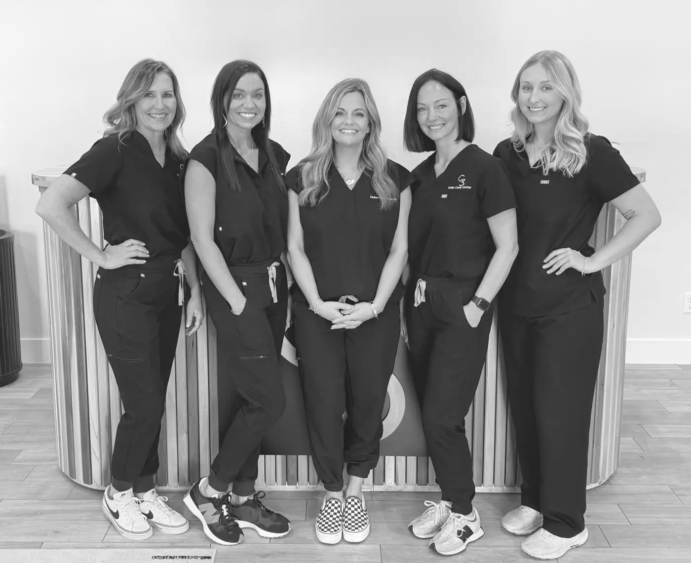 The five-person Cedar Creek Cosmo team in black studio scrubs, standing together at the wood-slat front desk